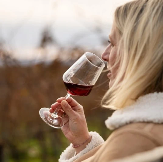 Kerstin Königshofer trinkt ein Glas Wein mit Blick auf Weingärten.